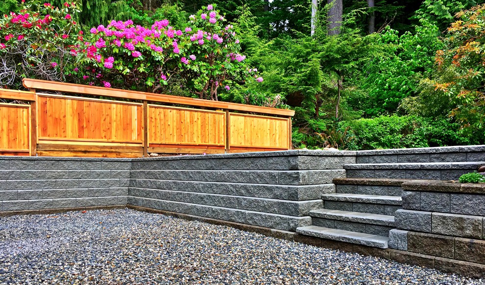 Modern backyard shaded garden in Vancouver with a retaining wall, gravel and a wood fence.