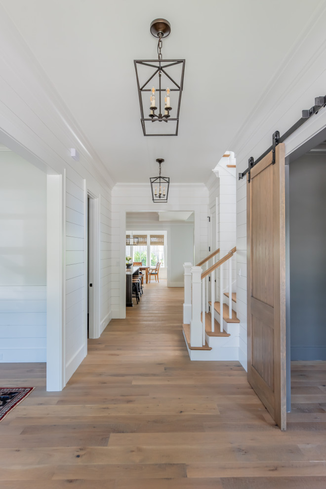 This is an example of a beach style entryway with white walls, light hardwood floors, a single front door, a medium wood front door and planked wall panelling.