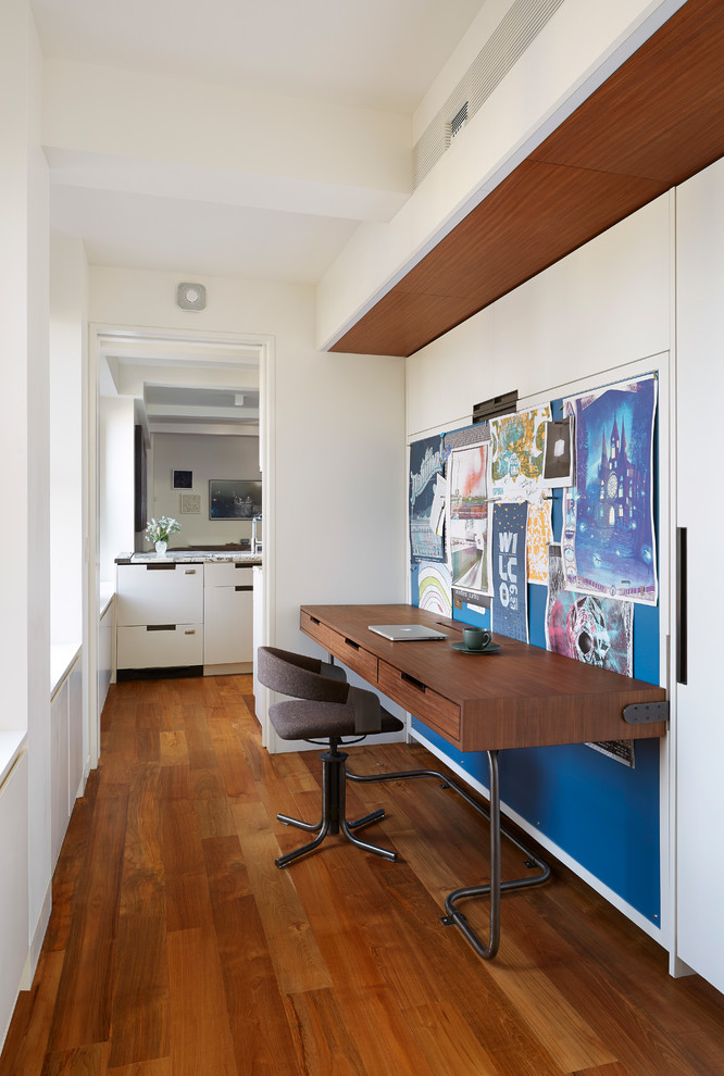 This is an example of a small contemporary study room in New York with white walls, medium hardwood floors and a built-in desk.