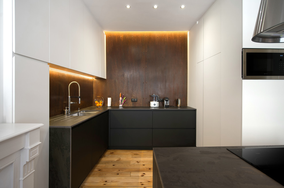 Inspiration for a large contemporary open plan kitchen in Toulouse with an undermount sink, black cabinets, marble benchtops, metallic splashback, black appliances, light hardwood floors, with island and black benchtop.