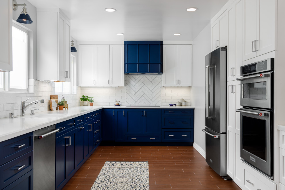 Inspiration for a large transitional u-shaped eat-in kitchen in Orange County with an undermount sink, shaker cabinets, quartz benchtops, white splashback, porcelain splashback, stainless steel appliances, porcelain floors, brown floor, white benchtop and blue cabinets.