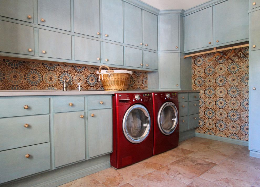 Photo of a large mediterranean l-shaped dedicated laundry room in Dallas with flat-panel cabinets, blue cabinets, a side-by-side washer and dryer, pink floor, limestone floors and multi-coloured walls.
