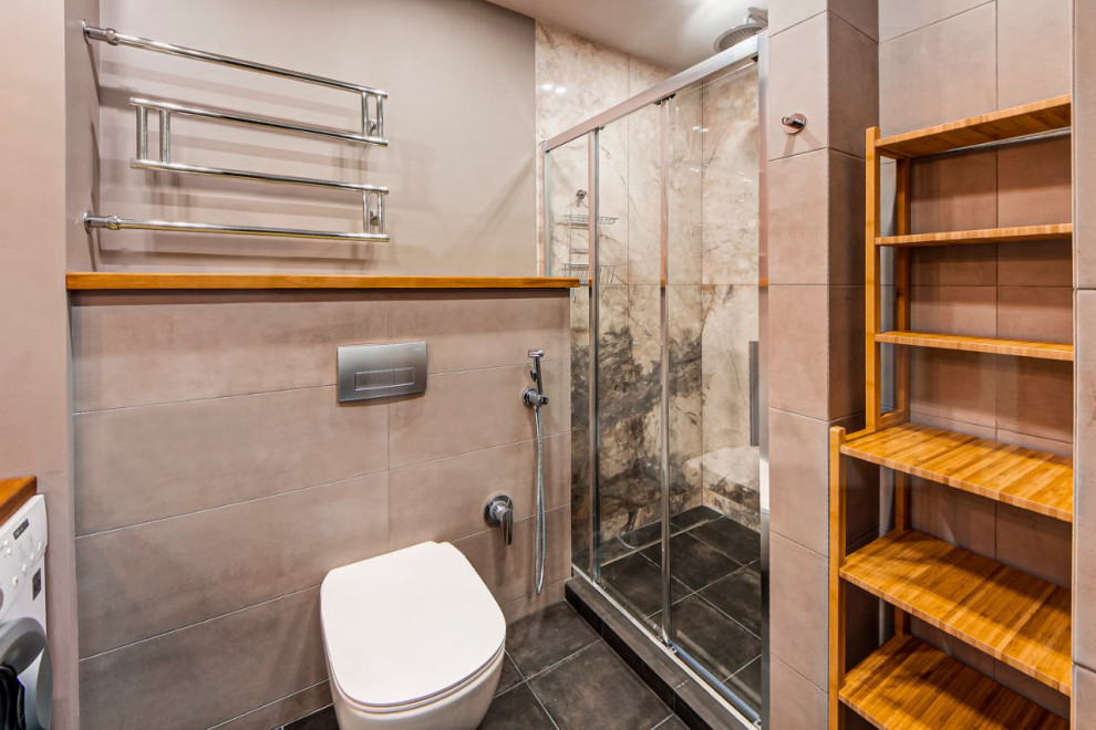 Exempel på ett litet industriellt beige beige badrum med dusch, med skåp i ljust trä, en dusch i en alkov, en vägghängd toalettstol, grå kakel, porslinskakel, grå väggar, klinkergolv i porslin, ett nedsänkt handfat, träbänkskiva, grått golv och dusch med skjutdörr