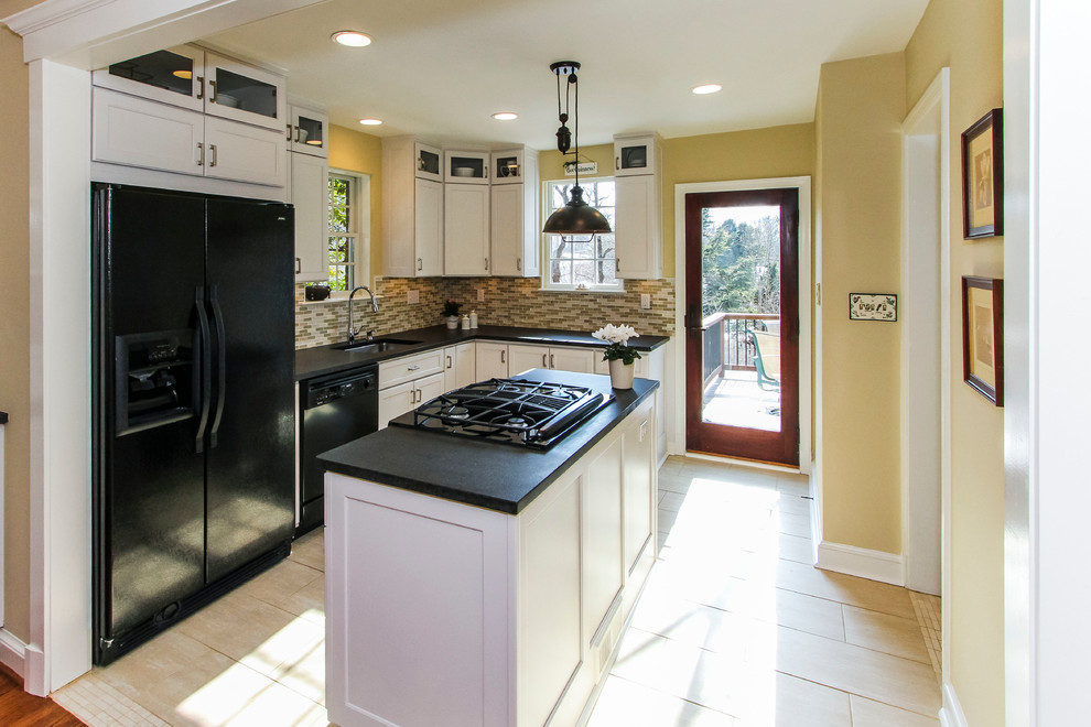 Photo of a mid-sized transitional l-shaped eat-in kitchen in DC Metro with an undermount sink, recessed-panel cabinets, white cabinets, solid surface benchtops, multi-coloured splashback, glass tile splashback, black appliances, porcelain floors, with island, beige floor and black benchtop.