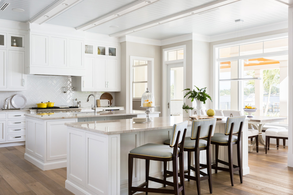 Design ideas for a large beach style galley eat-in kitchen in Miami with an undermount sink, shaker cabinets, white cabinets, quartzite benchtops, white splashback, panelled appliances, light hardwood floors, multiple islands and brown floor.