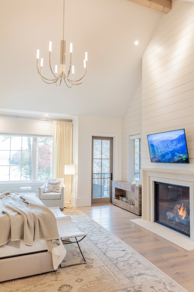 This is an example of a large beach style master bedroom in Other with white walls, light hardwood floors, a standard fireplace, white floor and vaulted.
