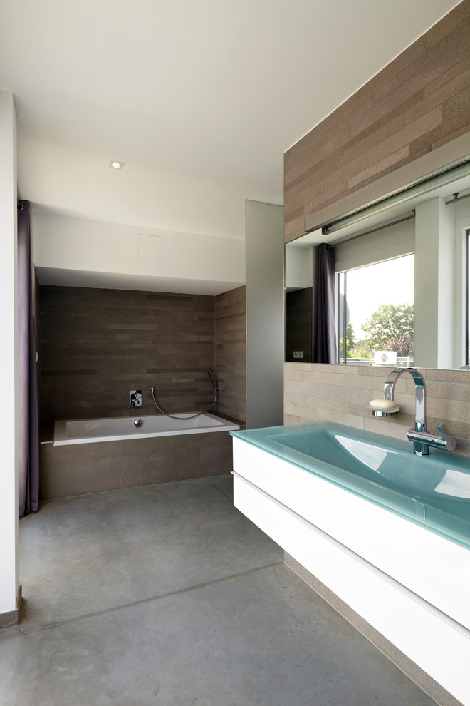 Photo of a large contemporary bathroom in Cologne with a trough sink, flat-panel cabinets, white cabinets, a drop-in tub, brown tile, concrete floors, a shower/bathtub combo, stone tile and white walls.