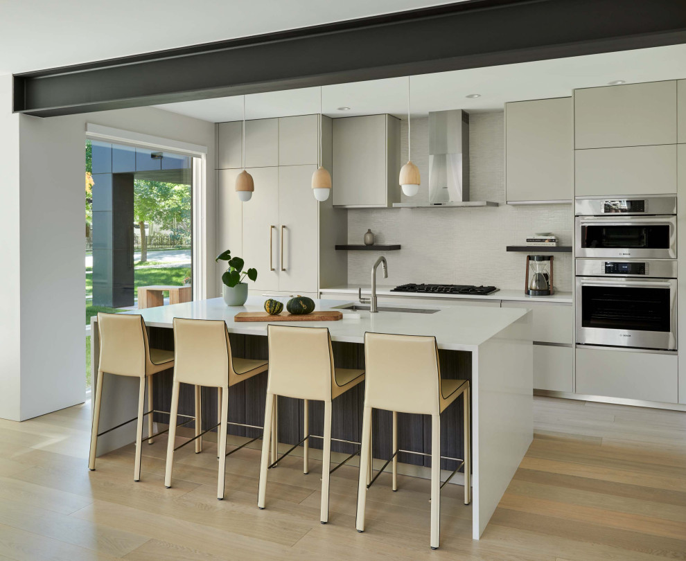 Inspiration for a mid-sized contemporary galley open plan kitchen in Denver with a drop-in sink, flat-panel cabinets, grey cabinets, quartz benchtops, beige splashback, stainless steel appliances, light hardwood floors, with island, brown floor and white benchtop.