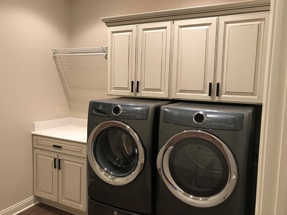 Photo of a large traditional single-wall dedicated laundry room in Milwaukee with raised-panel cabinets, white cabinets, solid surface benchtops, grey walls, dark hardwood floors, a side-by-side washer and dryer, brown floor and white benchtop.