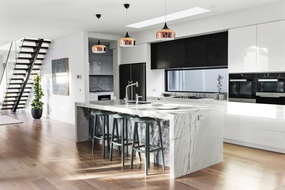 This is an example of a large modern galley kitchen in Melbourne with an undermount sink, marble benchtops, stainless steel appliances, light hardwood floors, beige floor and white benchtop.