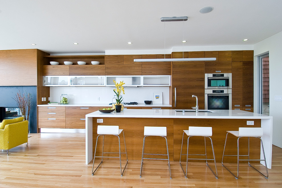 Mid-sized modern single-wall open plan kitchen in San Francisco with flat-panel cabinets, medium wood cabinets, white splashback, stainless steel appliances, a single-bowl sink, light hardwood floors and with island.