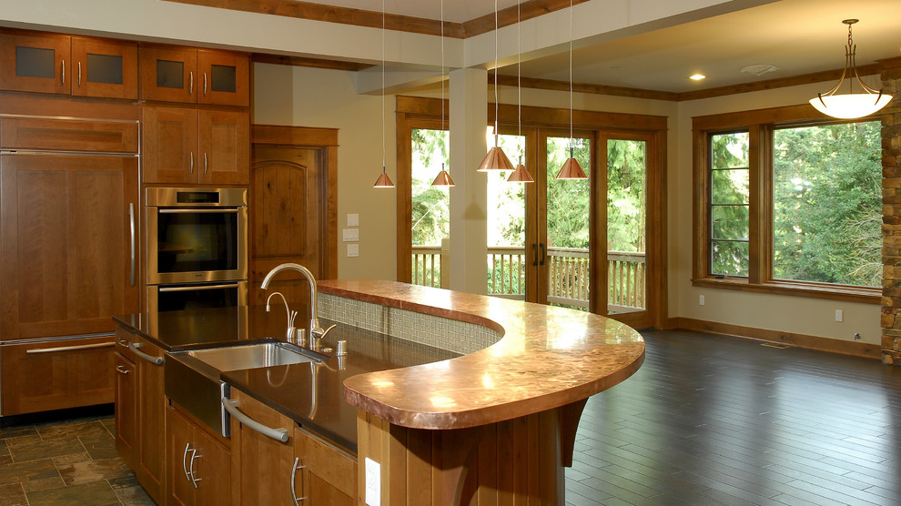 Photo of an arts and crafts eat-in kitchen in Seattle with a farmhouse sink, shaker cabinets, brown cabinets, copper benchtops, glass tile splashback and stainless steel appliances.