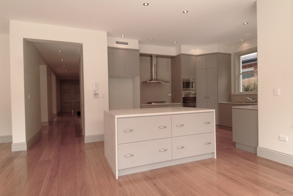 This is an example of a large contemporary u-shaped eat-in kitchen in Sydney with a drop-in sink, flat-panel cabinets, beige cabinets, limestone benchtops, beige splashback, stone slab splashback, stainless steel appliances, medium hardwood floors and with island.