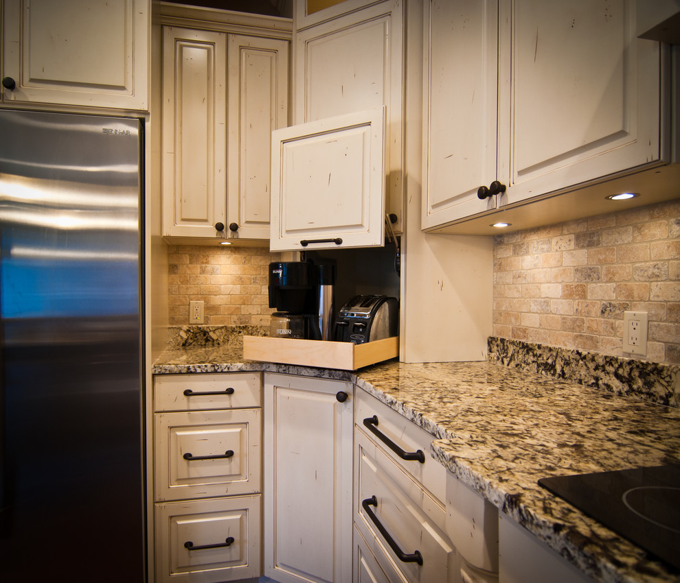 Mid-sized traditional l-shaped eat-in kitchen in Grand Rapids with a farmhouse sink, beaded inset cabinets, distressed cabinets, granite benchtops, beige splashback, ceramic splashback, stainless steel appliances, dark hardwood floors, with island, brown floor and multi-coloured benchtop.