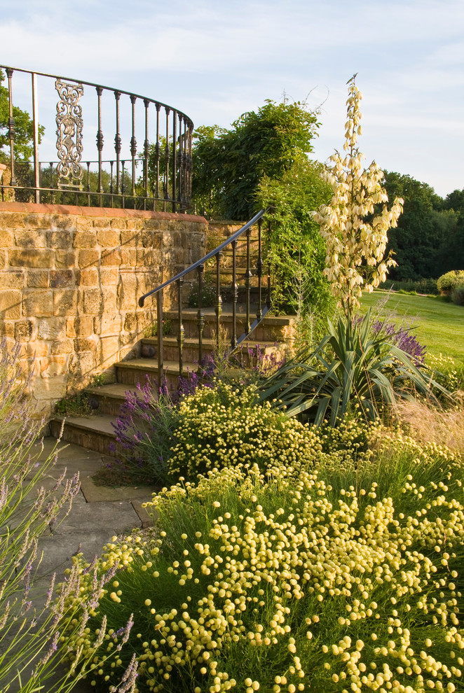 Large arts and crafts sloped full sun formal garden in Sussex with a retaining wall and natural stone pavers for summer.