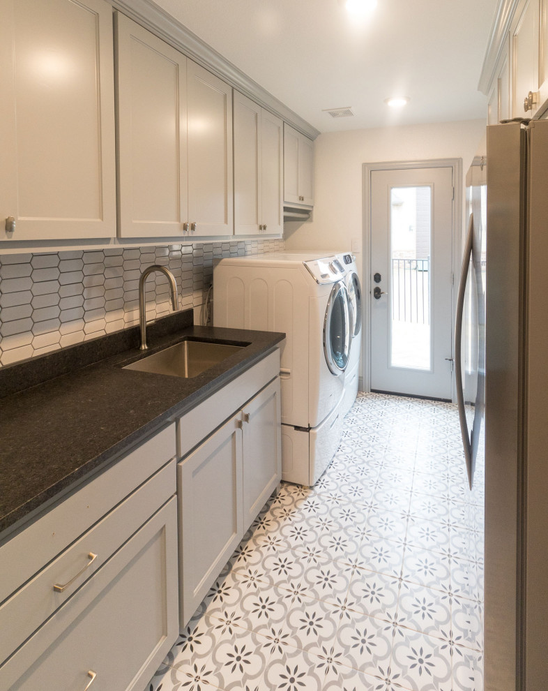Inspiration for a large transitional galley dedicated laundry room in Dallas with an undermount sink, shaker cabinets, grey cabinets, quartz benchtops, white splashback, mosaic tile splashback, grey walls, porcelain floors, a side-by-side washer and dryer, white floor and black benchtop.