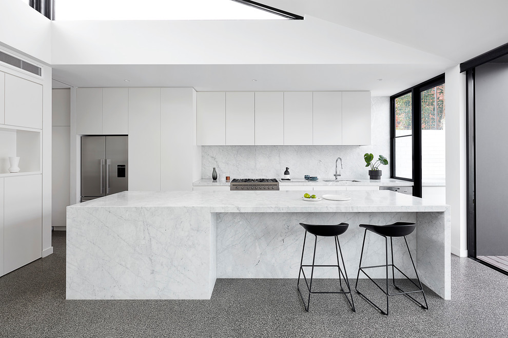 Photo of a large contemporary kitchen in Melbourne with an undermount sink, white cabinets, marble benchtops, white splashback, marble splashback, stainless steel appliances, concrete floors, with island, grey floor, white benchtop and flat-panel cabinets.