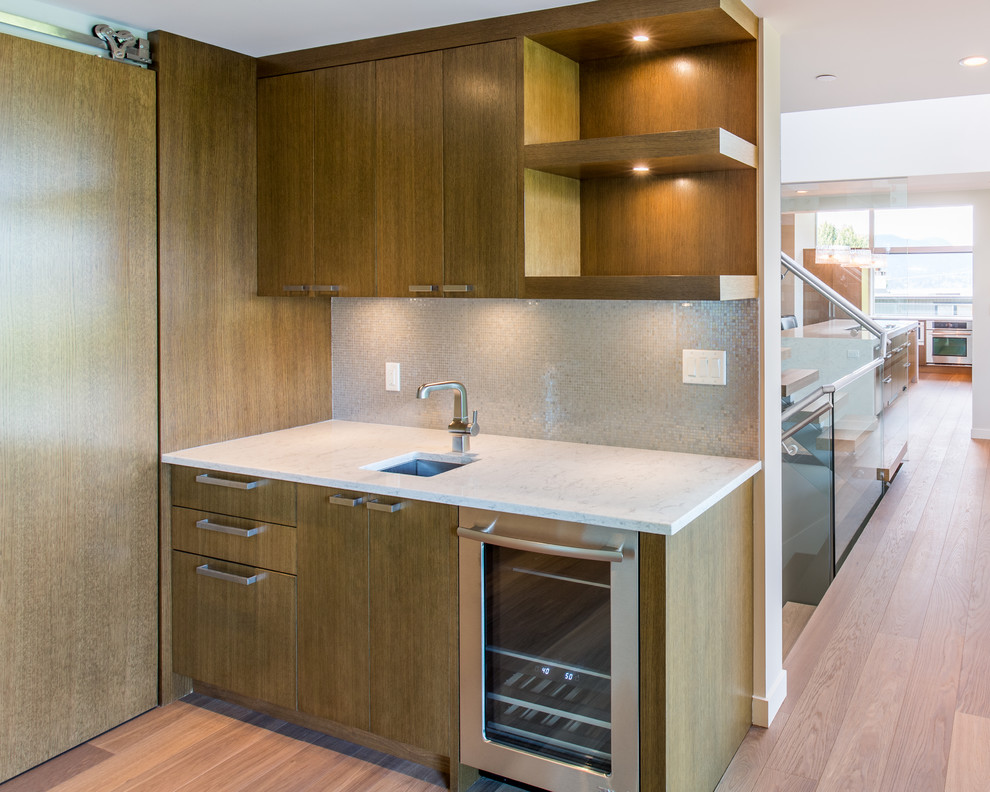 Mid-sized modern single-wall wet bar in Vancouver with flat-panel cabinets, medium wood cabinets, quartzite benchtops, white benchtop, an undermount sink, multi-coloured splashback, mosaic tile splashback, medium hardwood floors and brown floor.