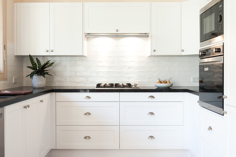 This is an example of a mid-sized contemporary u-shaped eat-in kitchen in Melbourne with an undermount sink, white splashback, subway tile splashback, stainless steel appliances, beaded inset cabinets, white cabinets, granite benchtops, light hardwood floors and no island.