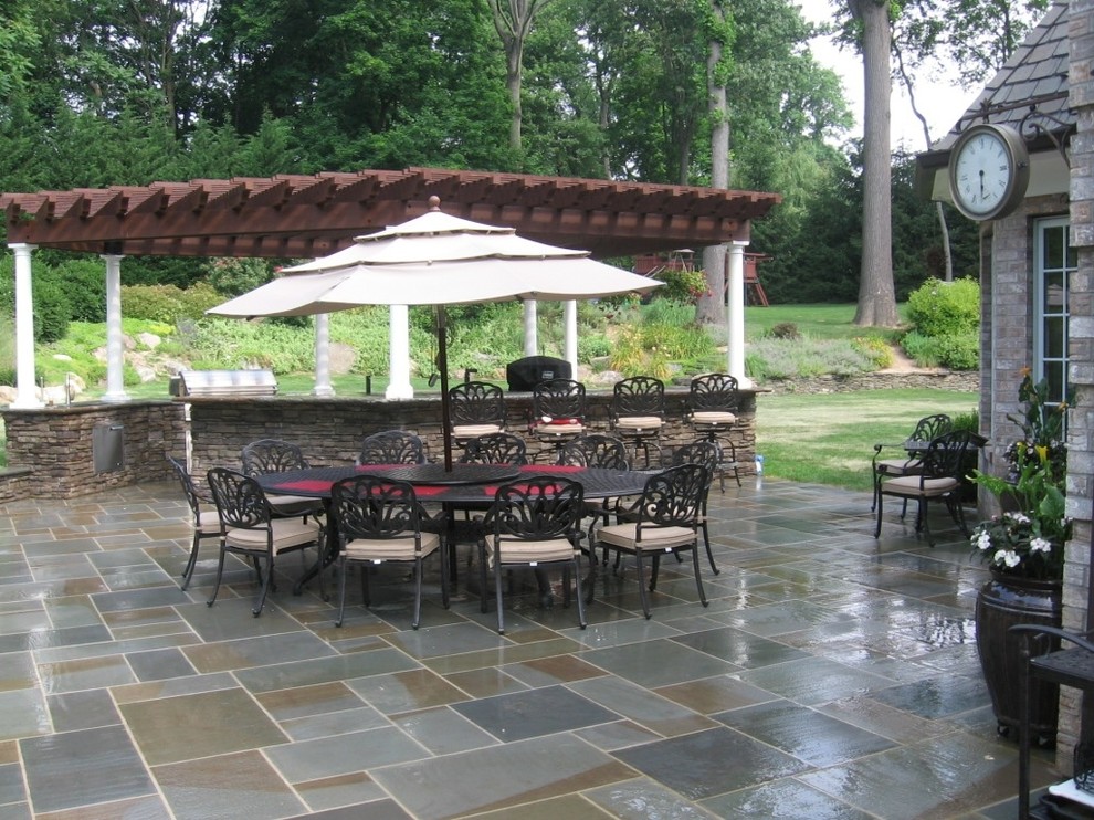 This is an example of a traditional backyard patio in New York with an outdoor kitchen, natural stone pavers and a gazebo/cabana.