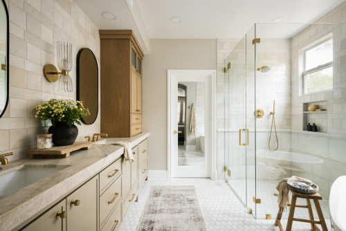 Luxurious bathroom with beige cabinets, stone countertop, glass shower enclosure, and brass fixtures for a warm, elegant design.