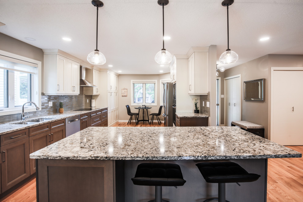 Inspiration for a mid-sized transitional single-wall medium tone wood floor and beige floor eat-in kitchen remodel in Edmonton with an undermount sink, shaker cabinets, beige cabinets, granite countertops, beige backsplash, glass tile backsplash, stainless steel appliances, an island and beige countertops
