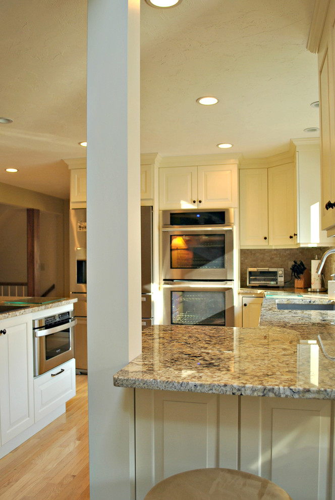 Mid-sized traditional l-shaped eat-in kitchen in Boston with an undermount sink, raised-panel cabinets, white cabinets, granite benchtops, beige splashback, stone tile splashback, stainless steel appliances, light hardwood floors and with island.