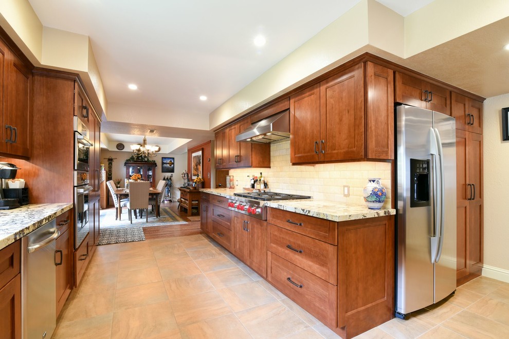 Large galley eat-in kitchen in San Luis Obispo with recessed-panel cabinets, medium wood cabinets, granite benchtops, white splashback, subway tile splashback, stainless steel appliances, a peninsula, an undermount sink, ceramic floors and beige floor.