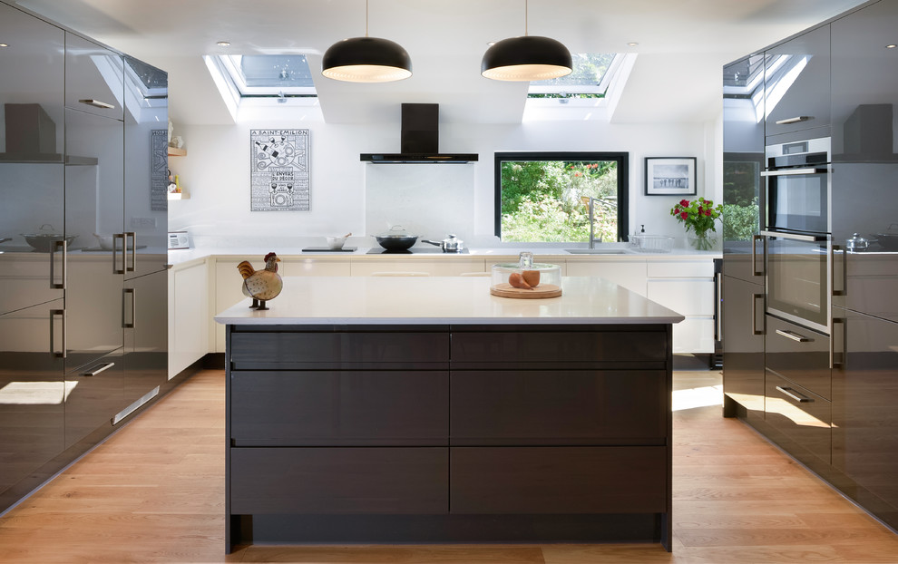 Design ideas for a large contemporary u-shaped eat-in kitchen in Cornwall with grey cabinets, granite benchtops, white splashback, with island, white benchtop, panelled appliances, brown floor, an undermount sink, flat-panel cabinets and medium hardwood floors.