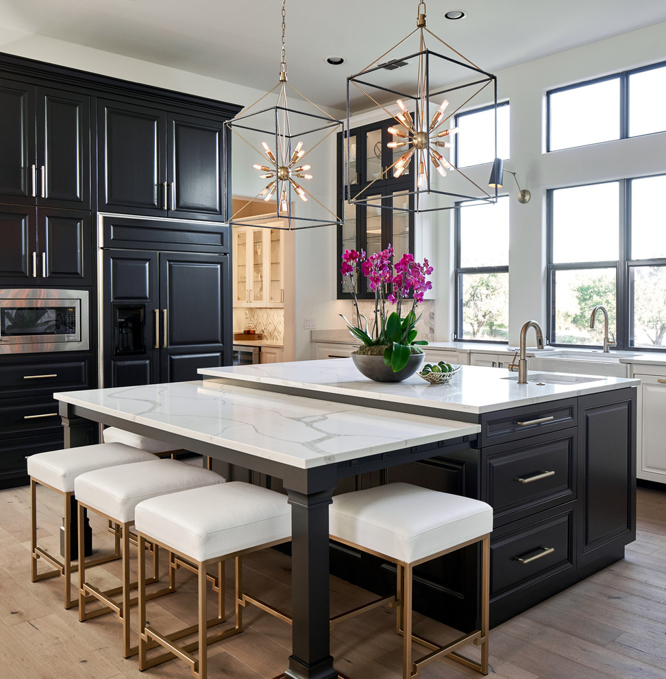 Design ideas for a large traditional kitchen in Austin with black cabinets, quartz benchtops, marble splashback, stainless steel appliances, light hardwood floors, with island, white benchtop and raised-panel cabinets.
