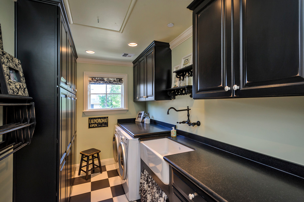 This is an example of a traditional laundry room in San Francisco with black cabinets, a farmhouse sink, multi-coloured floor and black benchtop.