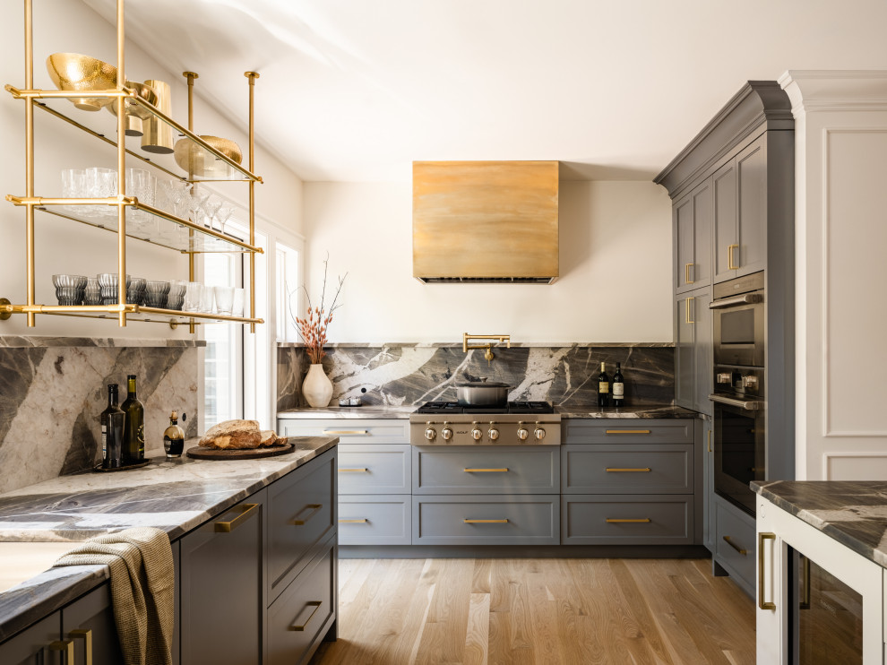 Inredning av ett klassiskt grå grått u-kök, med luckor med infälld panel, grå skåp, grått stänkskydd, stänkskydd i sten, rostfria vitvaror, mellanmörkt trägolv, en köksö och brunt golv