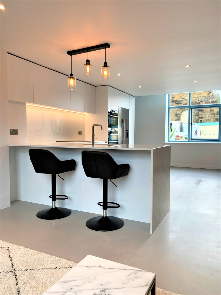 Bild på ett litet funkis kök, med släta luckor, vita skåp, bänkskiva i kvartsit, glaspanel som stänkskydd, rostfria vitvaror och betonggolv