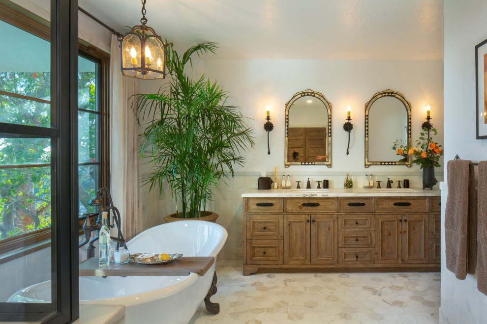 Design ideas for a mediterranean master bathroom in Los Angeles with recessed-panel cabinets, medium wood cabinets, a claw-foot tub, white tile, white walls, an undermount sink, white floor, white benchtops, a double vanity and a freestanding vanity.