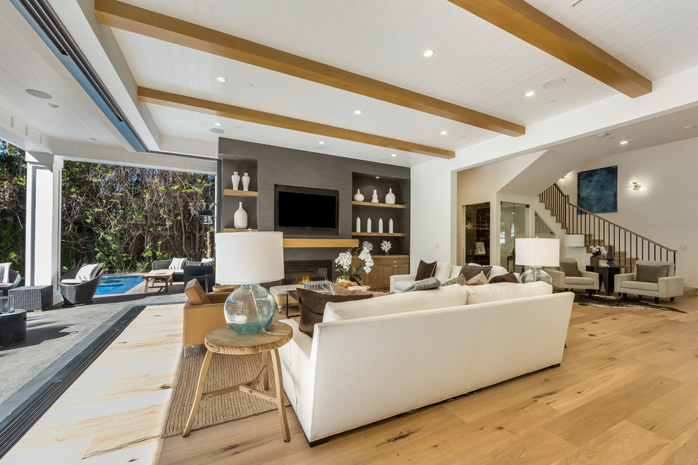This is an example of a large transitional open concept family room in Los Angeles with grey walls, light hardwood floors, a standard fireplace, a metal fireplace surround, a wall-mounted tv and brown floor.