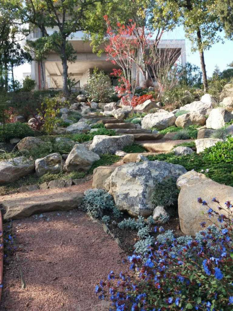 Design ideas for a large mediterranean sloped xeriscape full sun garden for summer in Other with a rockery and a stone fence.