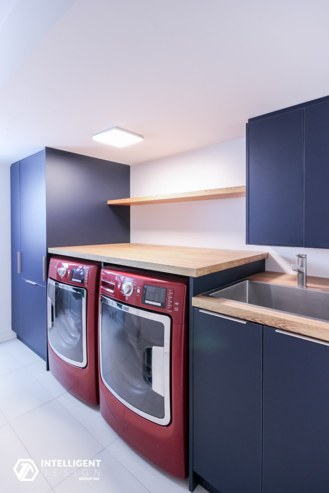Einzeilige, Mittelgroße Moderne Waschküche mit integriertem Waschbecken, flächenbündigen Schrankfronten, blauen Schränken, Arbeitsplatte aus Holz, weißer Wandfarbe, Keramikboden, Waschmaschine und Trockner nebeneinander, beigem Boden und oranger Arbeitsplatte in Toronto