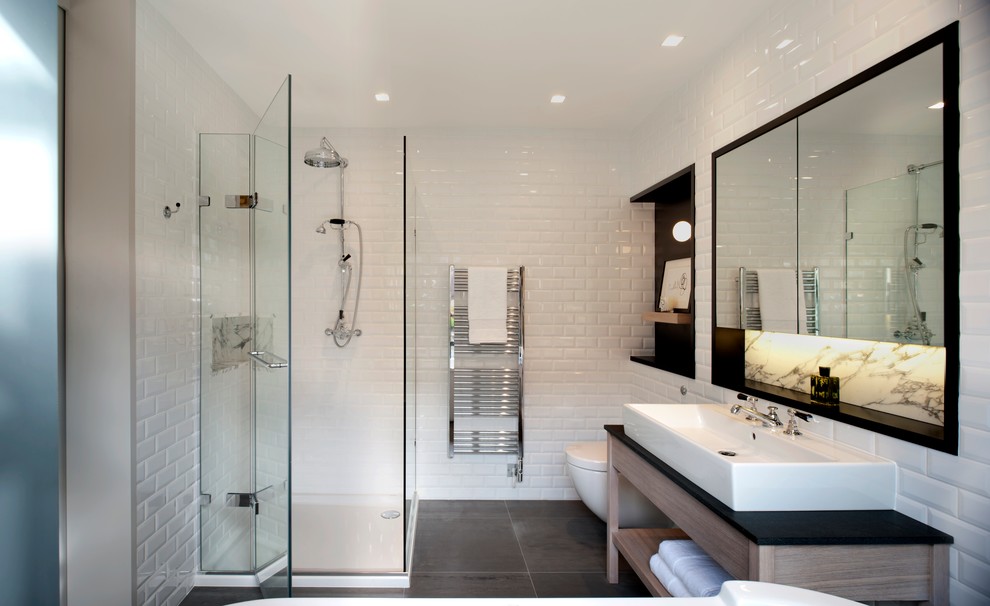 Photo of a mid-sized contemporary master bathroom in London with a console sink, a freestanding tub, a corner shower, a wall-mount toilet, white tile, porcelain tile and white walls.
