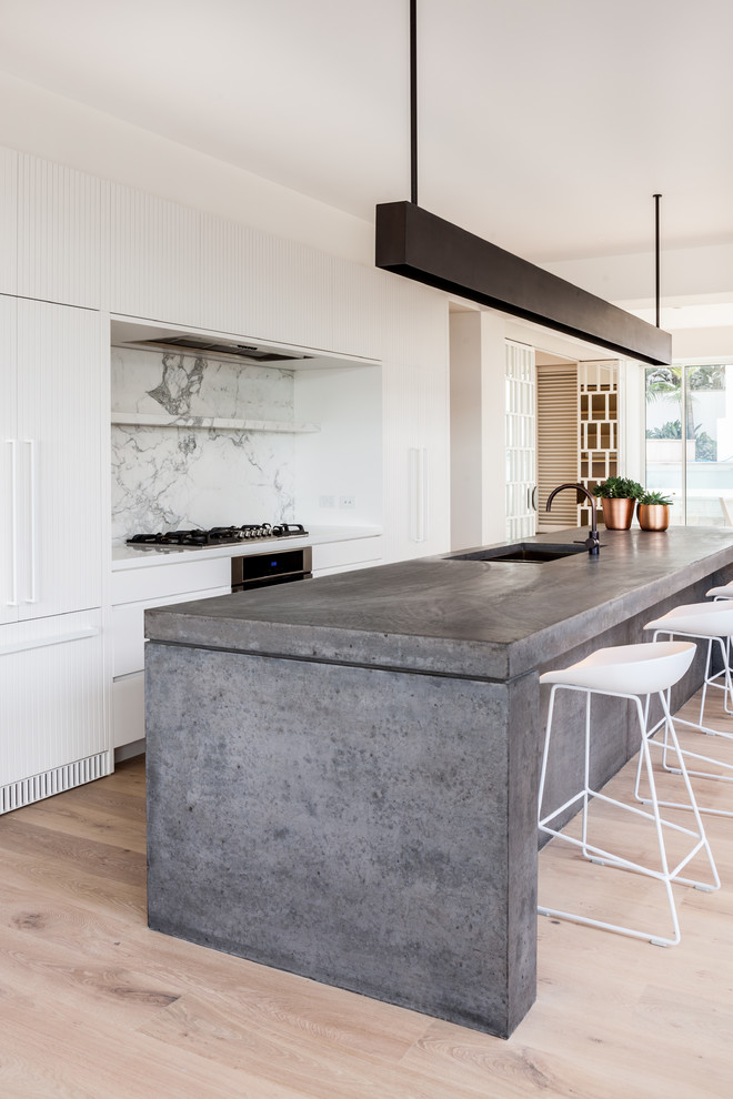 Inspiration for a contemporary galley kitchen in Sydney with an undermount sink, flat-panel cabinets, white cabinets, white splashback, stone slab splashback, panelled appliances, light hardwood floors, with island, beige floor and white benchtop.
