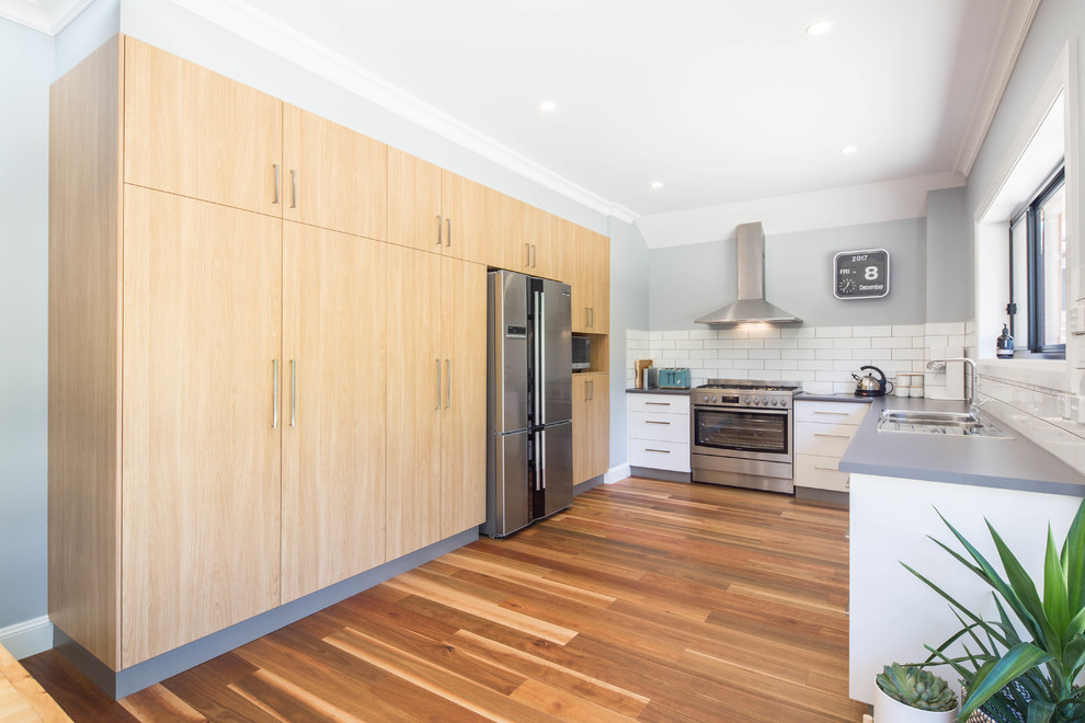 Mid-sized traditional u-shaped eat-in kitchen in Canberra - Queanbeyan with a drop-in sink, flat-panel cabinets, white cabinets, laminate benchtops, white splashback, porcelain splashback, stainless steel appliances, medium hardwood floors and beige floor.