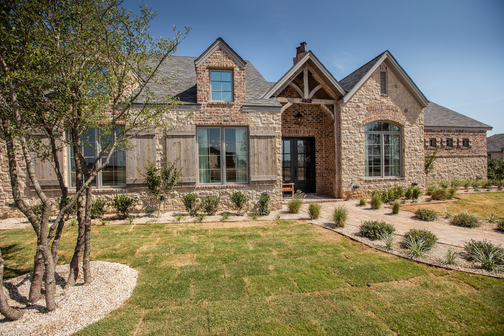 This is an example of a large country one-storey beige exterior in Austin with stone veneer and a gambrel roof.