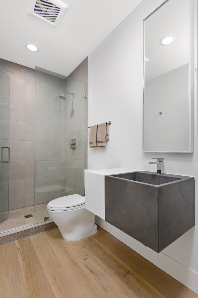 Large contemporary 3/4 bathroom with grey cabinets, a one-piece toilet, gray tile, porcelain tile, white walls, light hardwood floors, concrete benchtops, beige floor, a hinged shower door, grey benchtops, an alcove shower and an integrated sink.