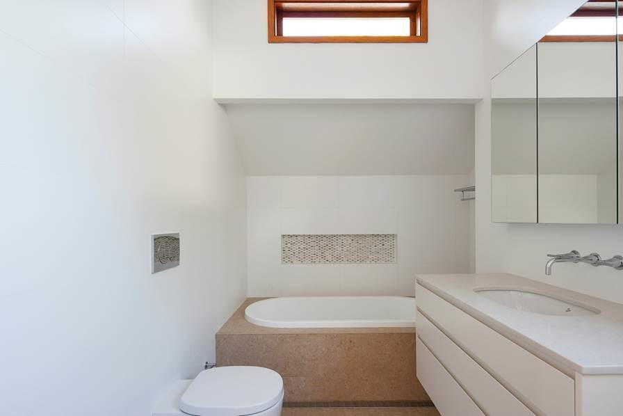 Design ideas for a mid-sized modern bathroom in Sydney with an undermount sink, flat-panel cabinets, white cabinets, engineered quartz benchtops, a drop-in tub, a corner shower, a wall-mount toilet, white tile, porcelain tile, white walls and travertine floors.