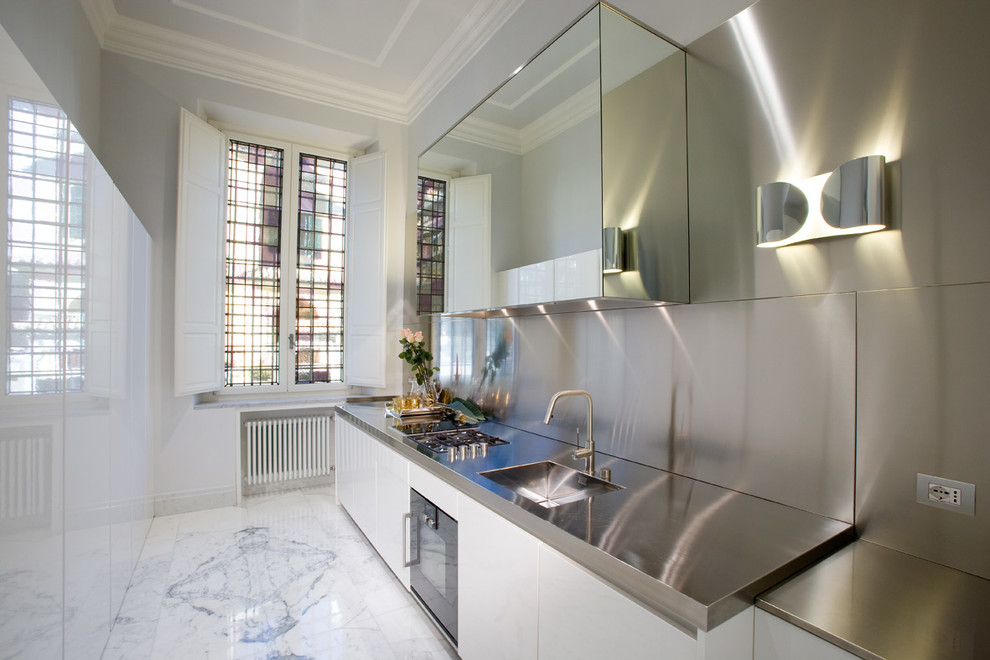 This is an example of a mid-sized contemporary single-wall separate kitchen in Rome with an integrated sink, flat-panel cabinets, white cabinets, stainless steel benchtops, metallic splashback, metal splashback, stainless steel appliances and marble floors.