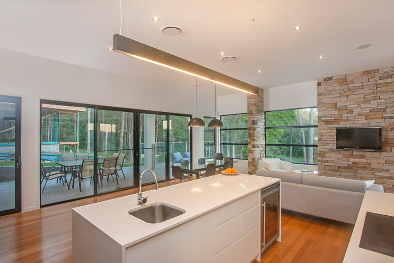 This is an example of a mid-sized contemporary l-shaped kitchen pantry in Sunshine Coast with a double-bowl sink, white cabinets, granite benchtops, white splashback, glass sheet splashback, stainless steel appliances, light hardwood floors and with island.