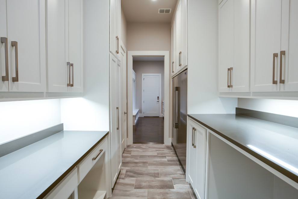This is an example of a large transitional galley utility room in Dallas with a single-bowl sink, shaker cabinets, white cabinets, granite benchtops, white walls, ceramic floors, a side-by-side washer and dryer and grey floor.