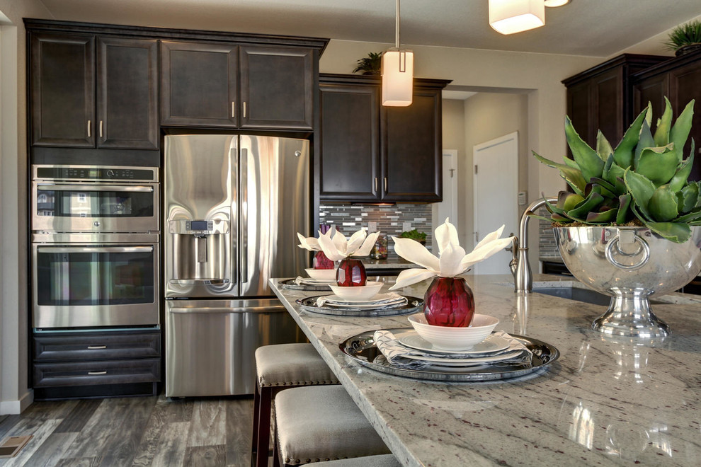 Mid-sized transitional l-shaped porcelain tile open concept kitchen photo in Denver with dark wood cabinets, granite countertops, stainless steel appliances, an island, an undermount sink, recessed-panel cabinets, white backsplash and mosaic tile backsplash