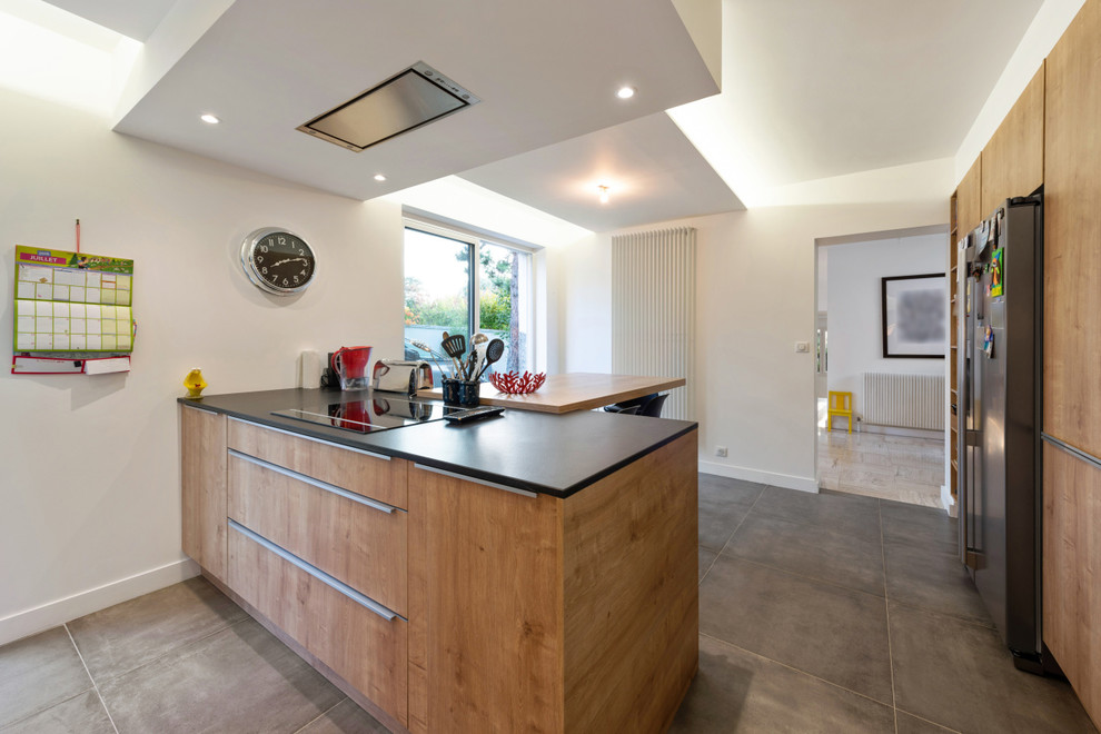 Photo of a mid-sized contemporary l-shaped eat-in kitchen in Lyon with an undermount sink, flat-panel cabinets, medium wood cabinets, black splashback, slate splashback, stainless steel appliances, travertine floors, with island, beige floor and black benchtop.