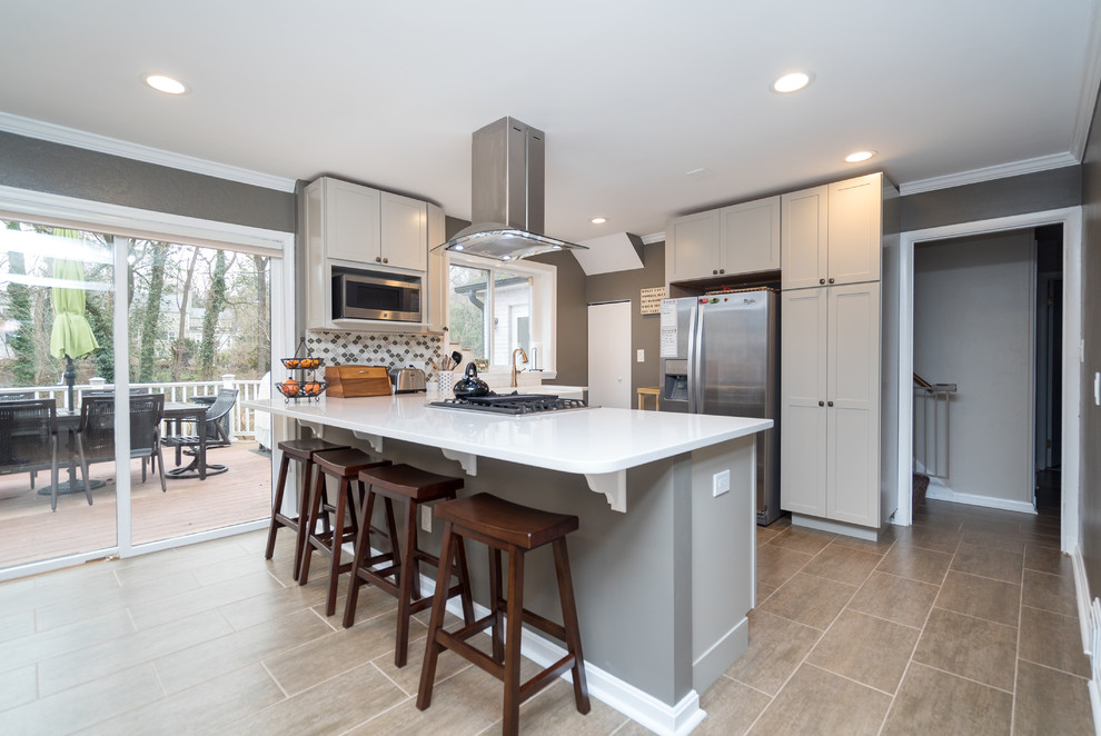 Mid-sized transitional l-shaped laminate floor open concept kitchen photo in DC Metro with a farmhouse sink, shaker cabinets, white cabinets, quartz countertops, gray backsplash, porcelain backsplash, stainless steel appliances and a peninsula