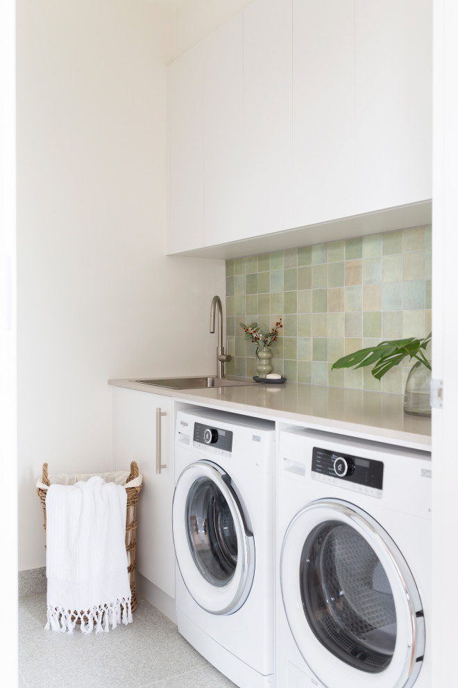Immagine di una piccola sala lavanderia minimal con lavello a vasca singola, ante bianche, top in quarzo composito, paraspruzzi verde, paraspruzzi con piastrelle a mosaico, lavatrice e asciugatrice affiancate, pavimento grigio e top grigio